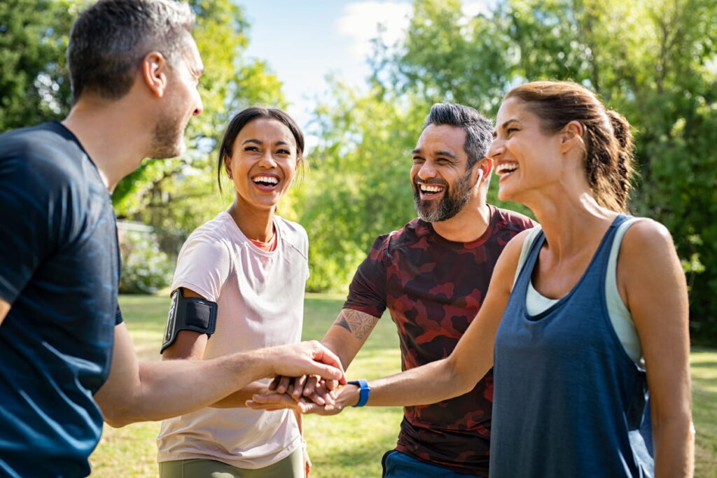 Group of active mature friends in park stacking hands