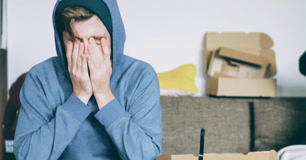 Adult sitting with hands covering face, showing stress and physical tension linked to psychosomatic symptoms