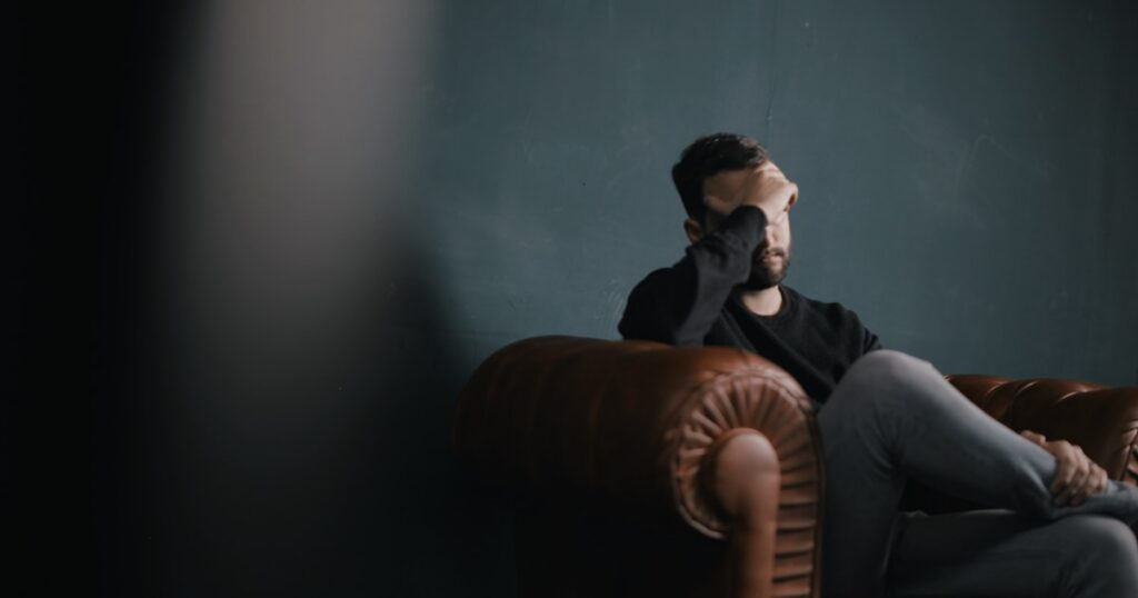 Adult man sitting alone with his hand over his eyes, representing the internal mental rumination of Pure O OCD